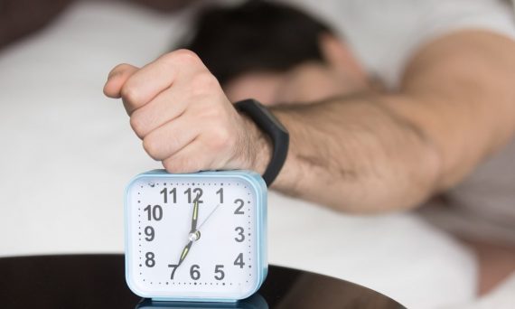 A man laying in bed with a clock on top of him